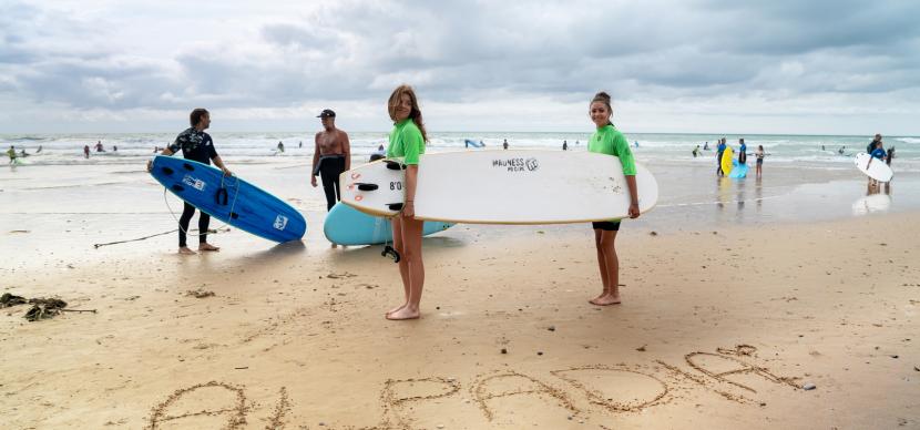two girls holding their surf boards on a beach