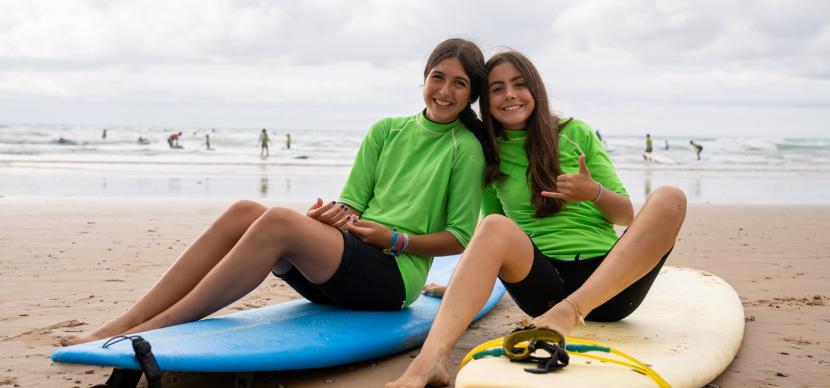 two girls sitting on their surfboards on a beach
